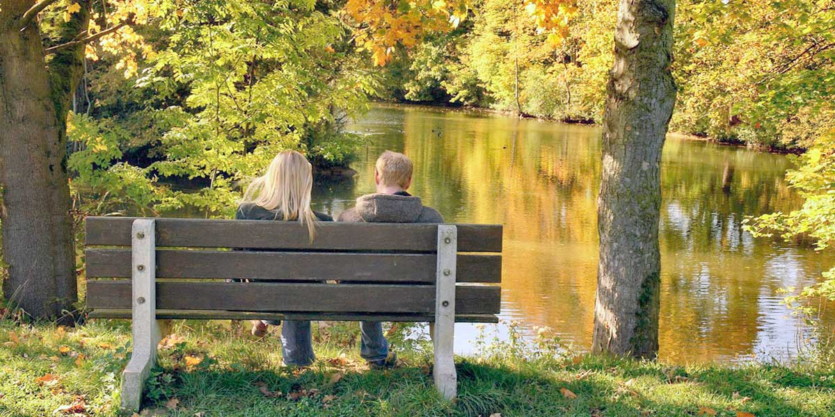 Пара сидит на лавочке у реки осенью